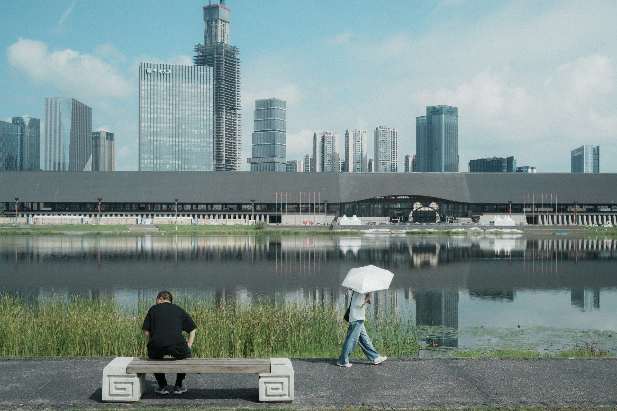 两个人停留在河岸草地上，水面另一侧是城市楼群