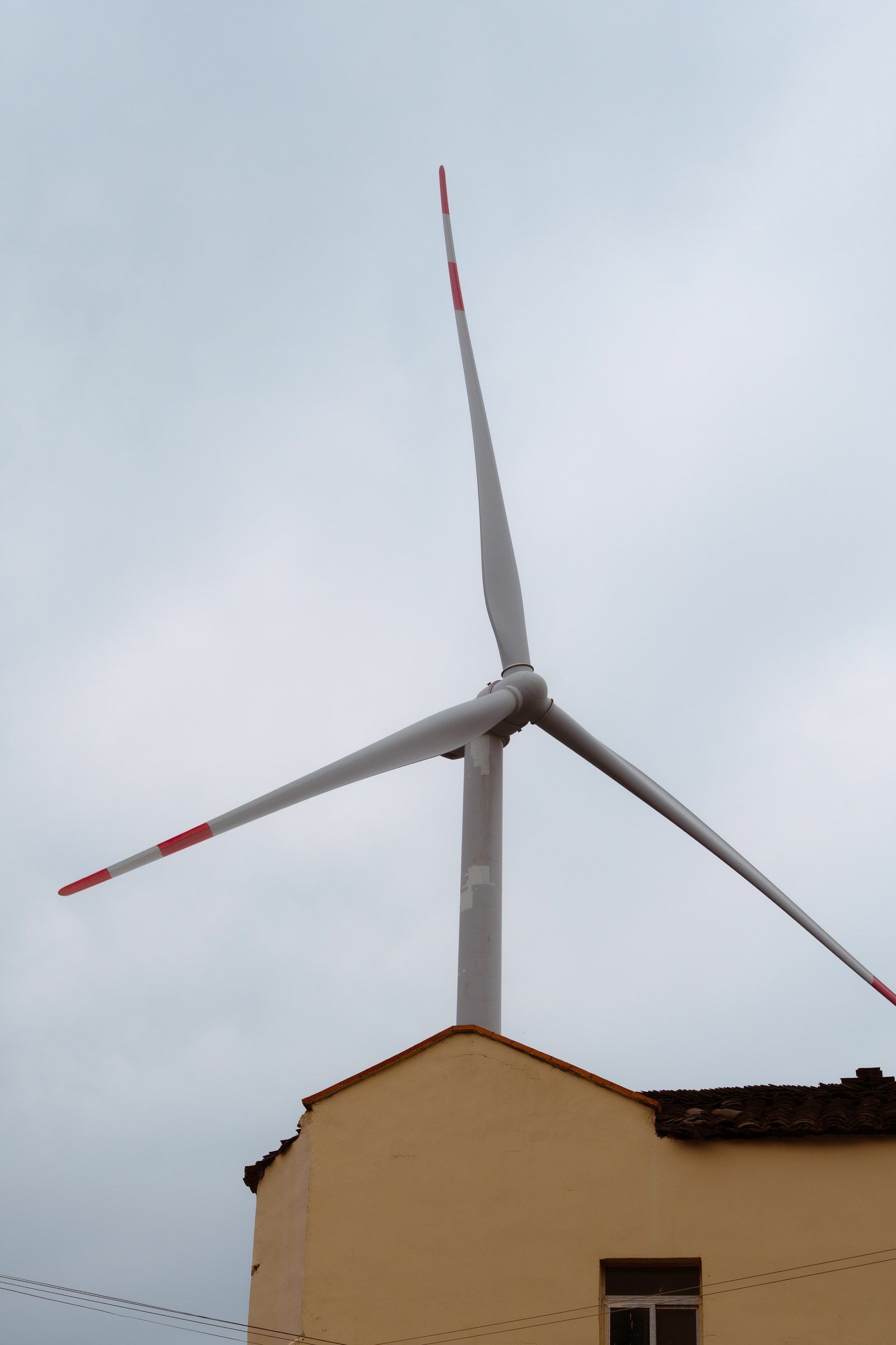 风力发电机立在山坡建筑后方的灰色天空里