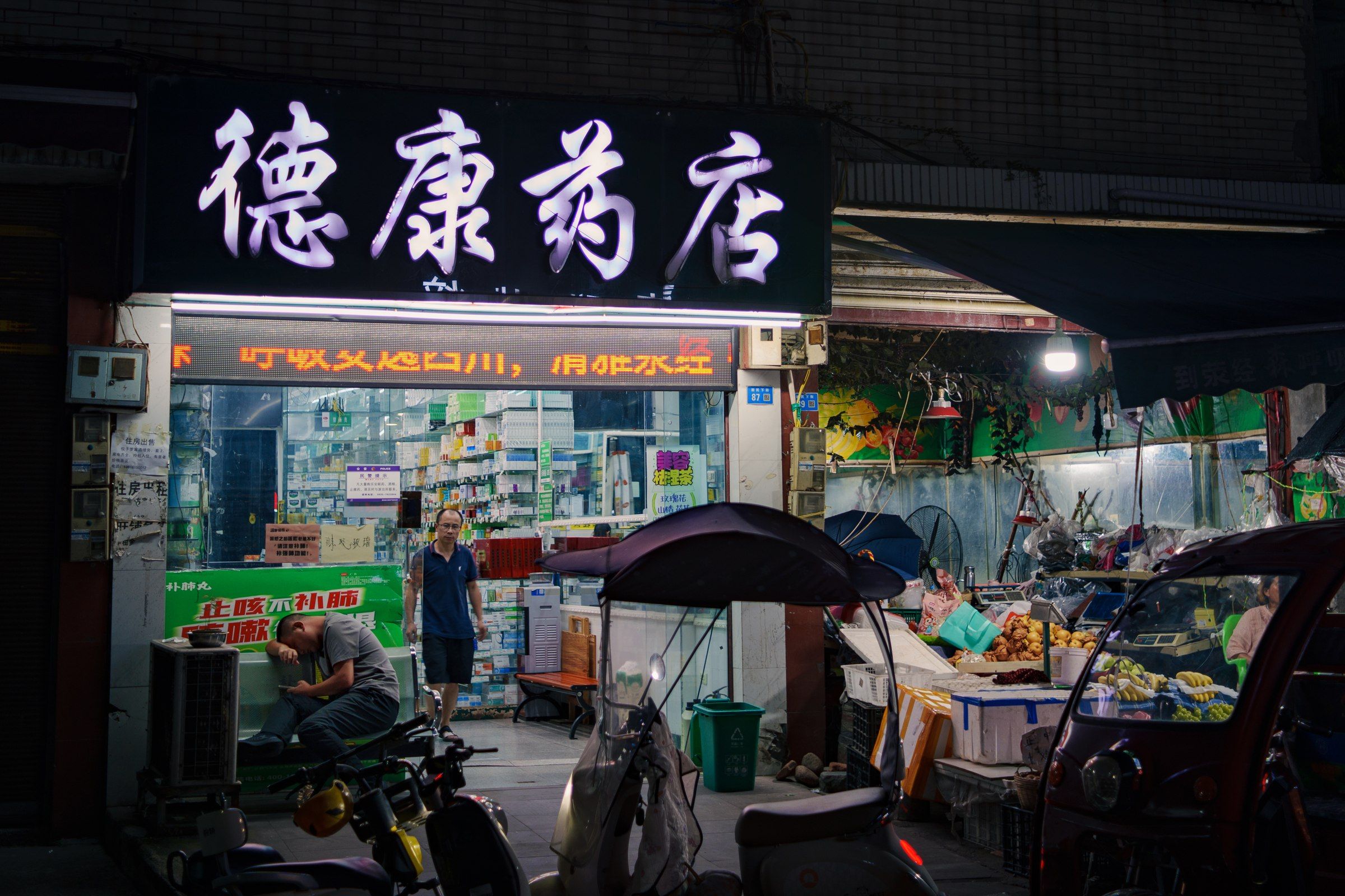 夜晚亮灯的街边药店，门前停着车辆