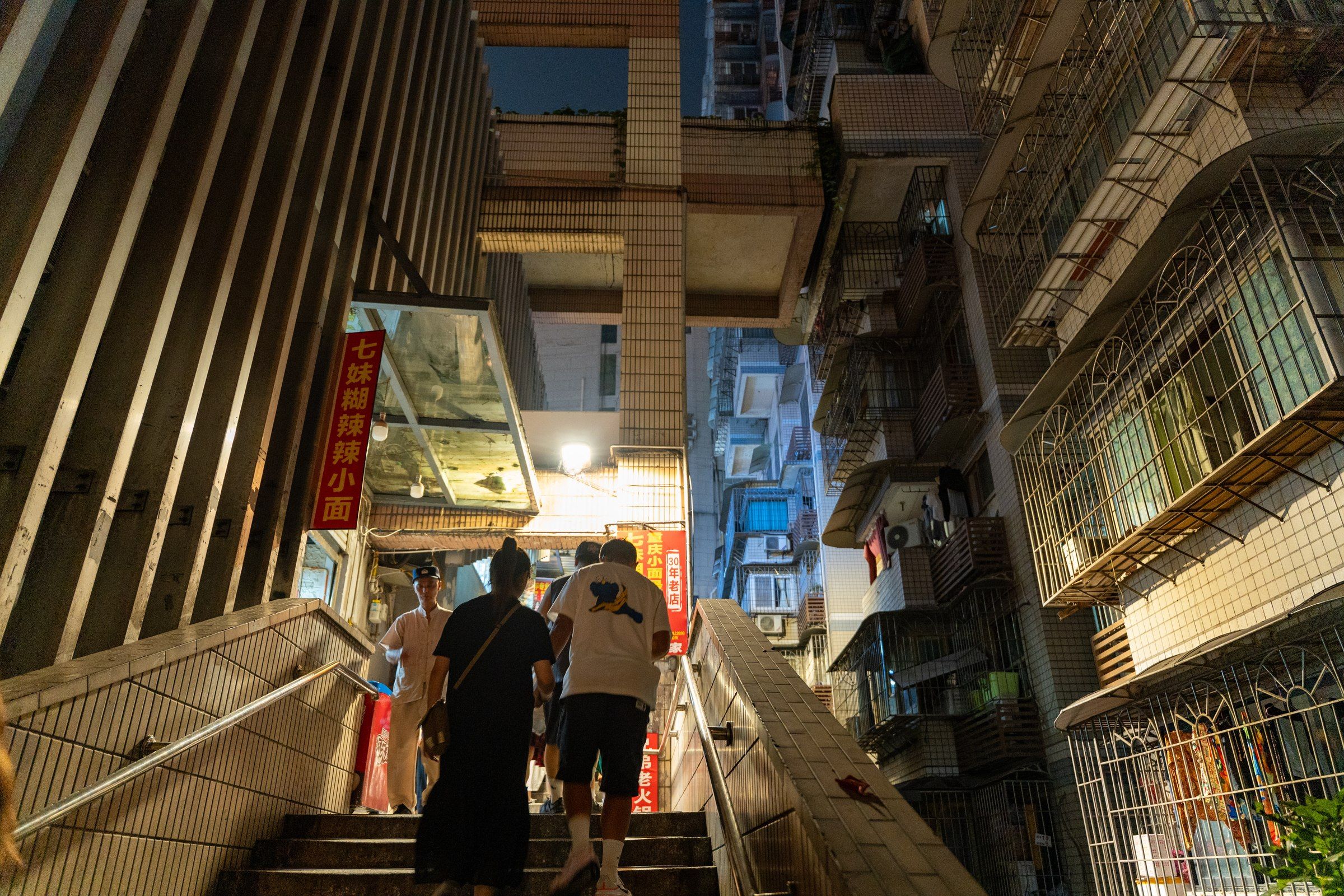 行人走上楼宇之间灯光交错的室外台阶